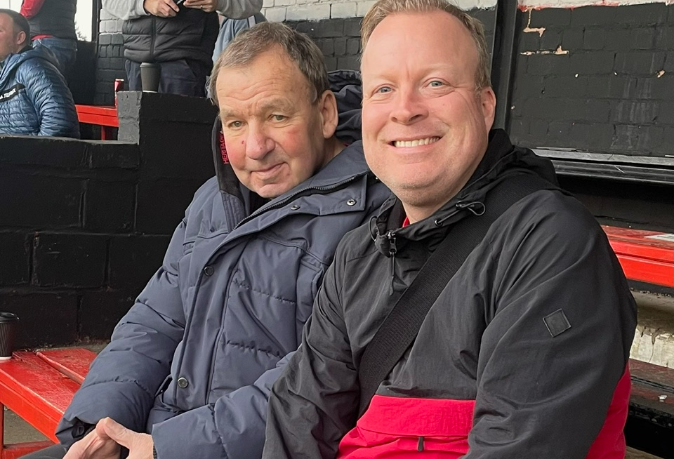 John Mills and David Watts in the stands at a recent home game for Maltby Main FC. Both are wearing big coats and are smiling